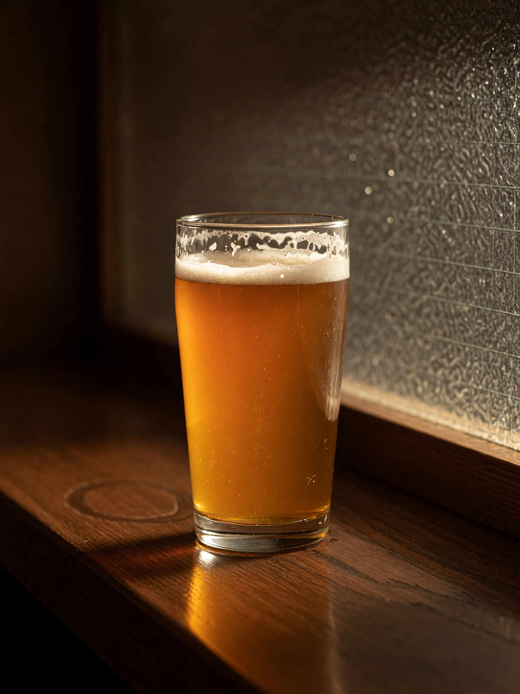Glas naturtrübes Zwickl-Bier auf dunklem Holztresen im warmen Lampenlicht